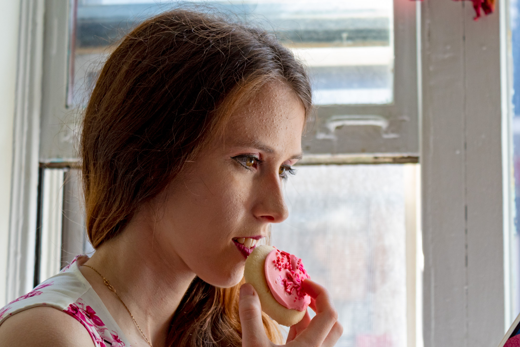 Woman holding a sugar cookie with pink frosting near her mouth