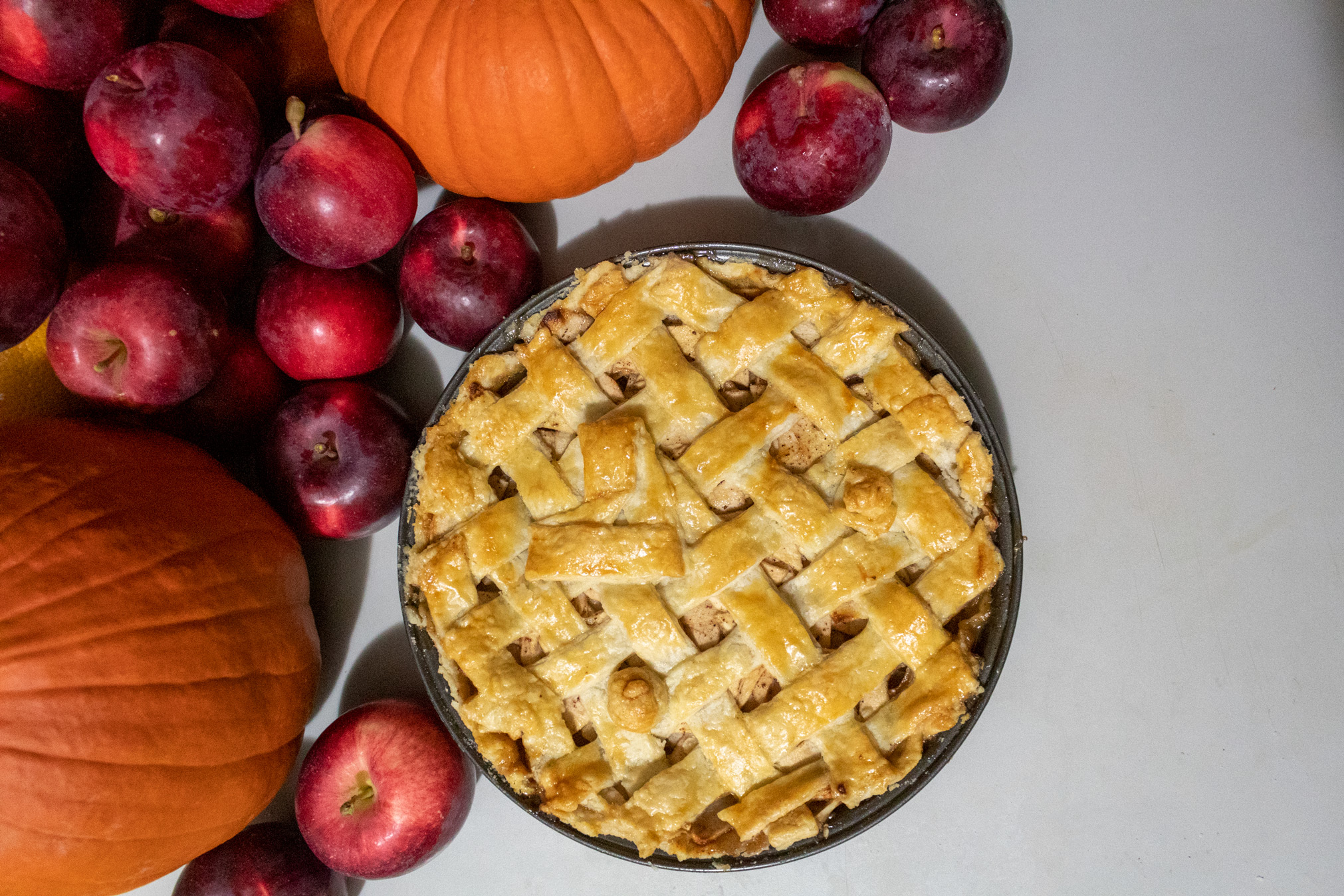 Apple pie with latticed top crust viewed from above surrounded by Spartan apples and pumpkins on the top and left
