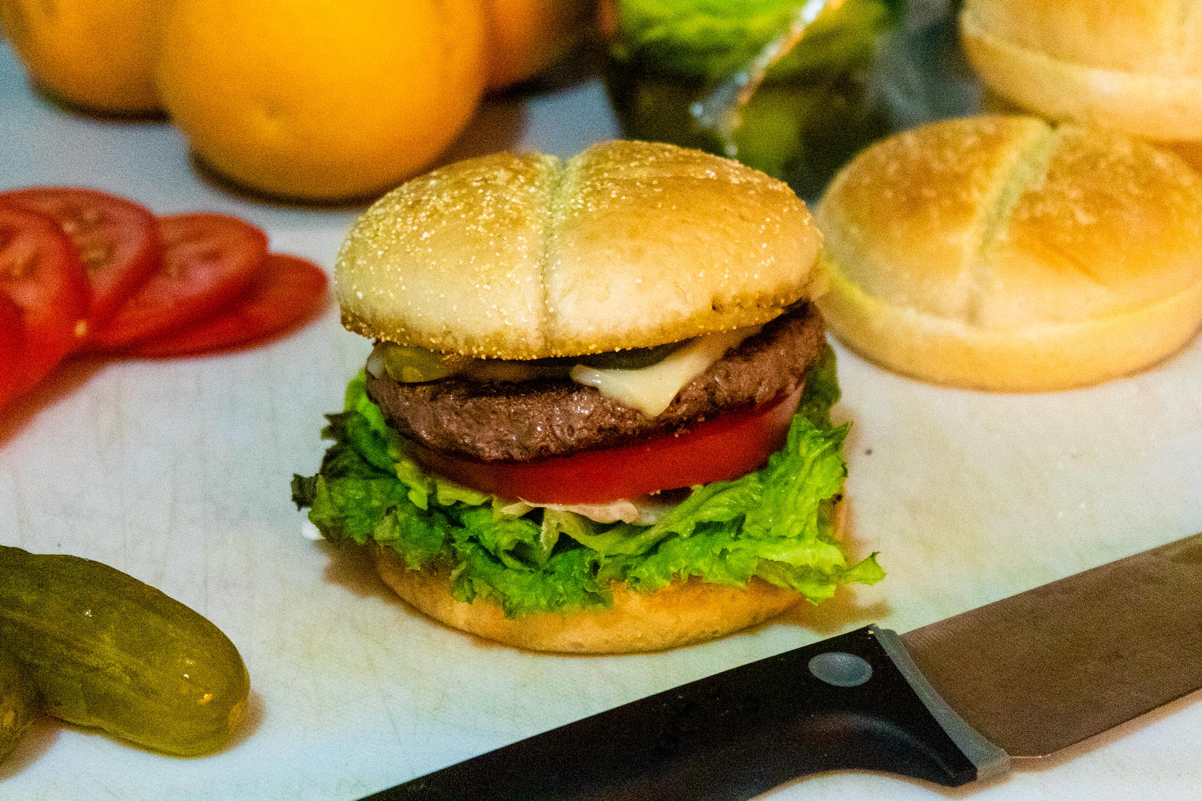 Hamburger with lettuce, tomatoes, cheese, and pickles surrounded by ingredients